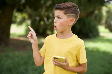 Stunned Caucasian little kid boy wearing yellow T-shirt standing outdoors points sideways right...