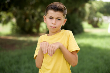 beautiful Caucasian little kid boy wearing stripped T-shirt standing outdoors makes bunny paws and...