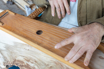 A man in ethnic clothes plays an ancient musical instrument. A man in a brown linen quilted jacket plays the psaltery.