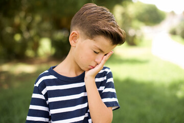 beautiful Caucasian little kid boy wearing stripped T-shirt standing outdoors with sad expression covering face with hands while crying. Depression concept.