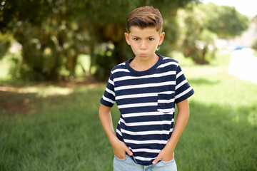 Portrait of lovely funny beautiful Caucasian little kid boy wearing stripped T-shirt standing outdoors sending air kiss