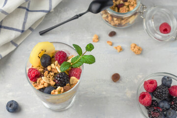 A glass of muesli, berries and yoghurt parfait on the table. Healthy breakfast. Granola with raspberries, blueberries, golden kiwi and mint sprig. Vegan natural dessert.