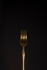 Close-up of a stylish steel gold fork on a dark background. Vertical position. Copy space.