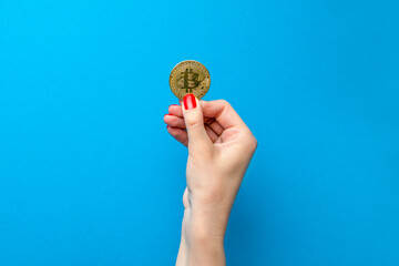 bitcoin in hand, female hand holds a gold bitcoin coin. Cryptocurrency value, digital money, space for text. Blue background.