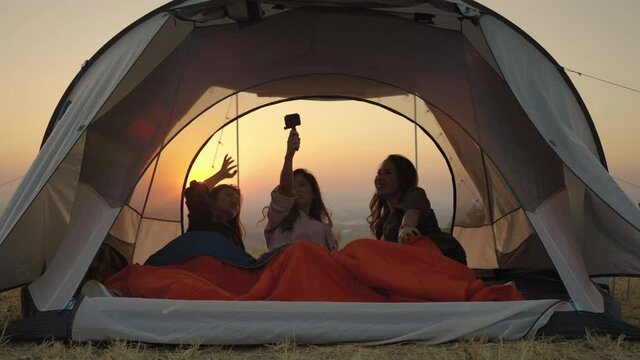 girl friend group Asians laying in tents during camping are waking up to watch the sun rise and shoot video from their action cams to show off to their friends in social media, the concept of adventur