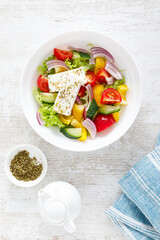 Fresh summer vegetable salad with lettuce, tomato, cucumber, bell pepper, onion and feta cheese, dressed with olive oil. Top view