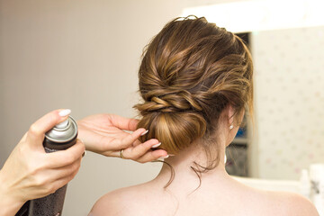 Naklejka premium The stylist performs the hairstyle, hair styling in the salon. Splashes hairspray.