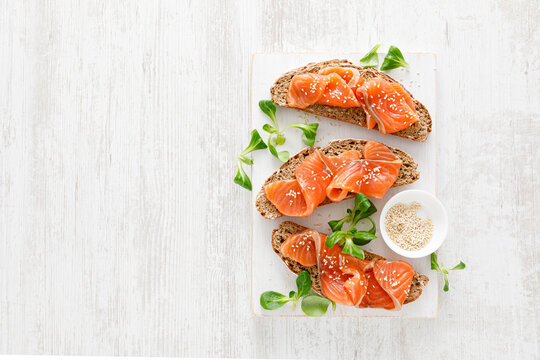 Whole grain rye bread open sandwiches with salted salmon on a white rustic wooden table. Healthy food. Top view