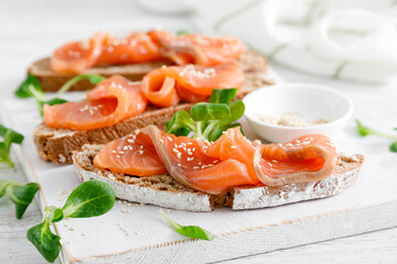Whole grain rye bread open sandwiches with salted salmon on a white rustic wooden table. Healthy food - obrazy, fototapety, plakaty