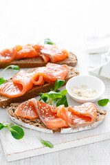 Whole grain rye bread open sandwiches with salted salmon on a white rustic wooden table. Healthy food