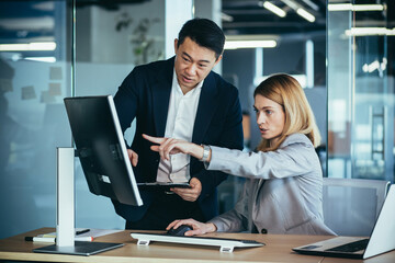 Two Asian male and female colleagues in a modern office, a woman shows the work done on the monitor, consults and discusses