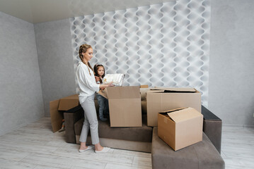 A young mother with children unpacks a box of things after moving to a new apartment. Purchase of real estate. Housewarming, delivery and transportation of goods.