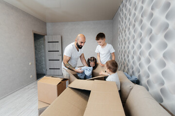 A young father with children unpacks a box of things after moving to a new apartment. Purchase of real estate. Housewarming, delivery and transportation of goods.