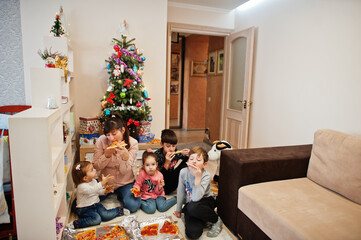 Happy family with four kids eating pizza at home.