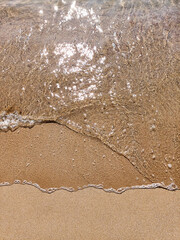 Small see clear waves on sand beach summer day. Top view. Ocean clear water seafoam, yellow sand. Summer background. Nature relax concept, holiday vacation. Template for social networks stories