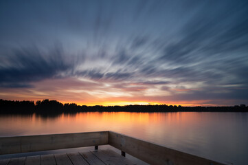 Panoramic Tranquil golden hour cloud above the forest lake at sunset. Dramatic cloudscape. Long exposure on the water