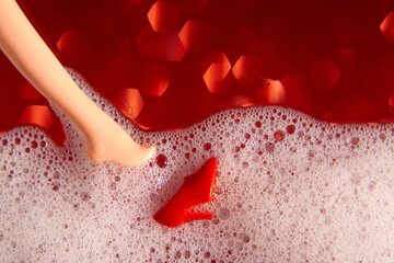 Blurred red glittering background. White foam, doll's foot and red.