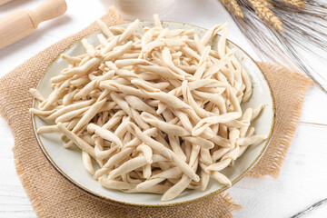 Whole grain wheat raw apulian pasta called Pizzarieddi or maccaruni on a ceramic plate on white wooden table. Fresh maccheroni typical dish of Puglia, Salento Italy. Italian homemade pasta background
