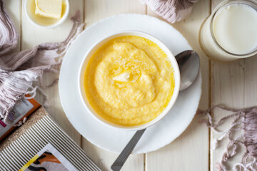 Healthy breakfast: milk corn porridge in a white plate on a white table. Top view.