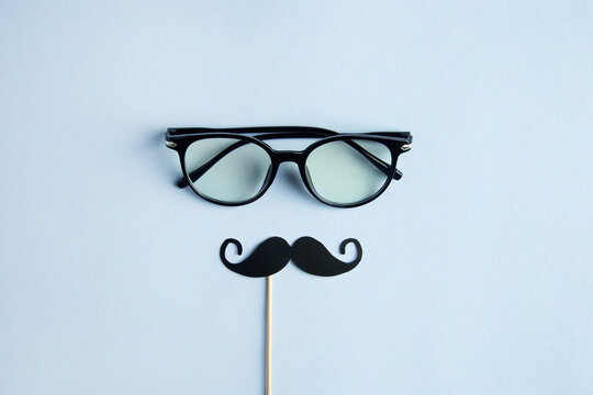 Father's Day Holiday Concept. Transparent glasses, stylish black paper photo booth props moustaches on blue background. 