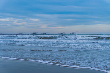 Fototapeta na wymiar Scena con il mare con le onde e la spiaggia e dei padelloni sullo sfondo a Marina di Ravenna, in Italia, in inverno. Viaggiare. Vacanze. Destinazione. Paesaggio marino.
