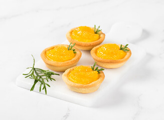 Small Tartlets with custard and slices of tangerines covered with syrup on a serving board on a white background
