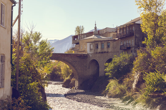 Akhty village, Dagestan, Russia. View of the stone arched bridge Usta Idrisan Muig and the Akhtychay river. Buildings of the village of Akhty