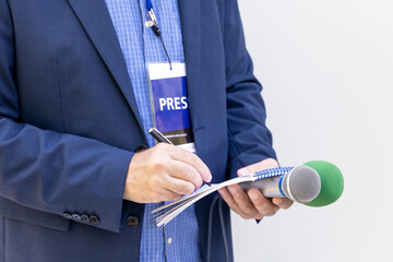 Journalism concept. Journalist wearing press pass at news conference or media event, holding...