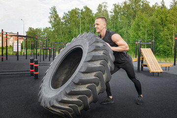 Obraz na płótnie Canvas Muscular bearded tattooed fitness man moving large tire in street gym.