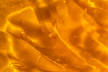 Texture of transparent yellow gel with air bubbles and waves on orange background. Concept of skin moisturizing, body care and prevention of covid19. Liquid beauty product closeup. Backdrop, flat lay