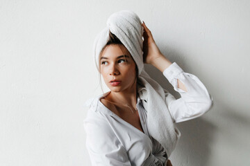 Obraz premium Portrait of a young woman with a towel on her head having slow self care morning. Young woman with hair wrapped in towel indoors, looking too the side