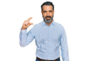 Middle aged man with beard wearing business shirt smiling and confident gesturing with hand doing small size sign with fingers looking and the camera. measure concept.