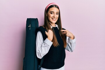 Beautiful brunette young musician woman wearing guitar case smiling happy pointing with hand and finger