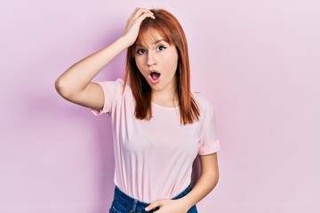 Obraz na płótnie Canvas Redhead young woman wearing casual pink t shirt surprised with hand on head for mistake, remember error. forgot, bad memory concept.