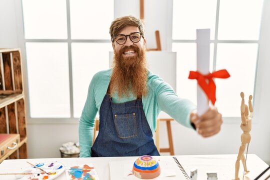Young redhead man smiling confident holding diploma at art studio