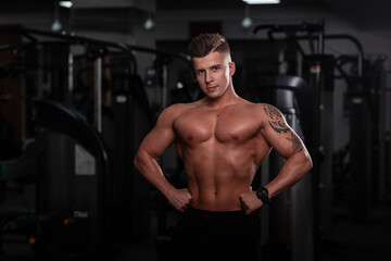 Obraz na płótnie Canvas Strong handsome fitness model man with a sports body and tattoo on hand does a workout in the gym