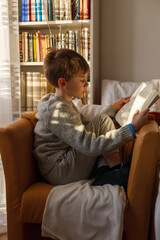 A boy sitting in an armchair and reading a book