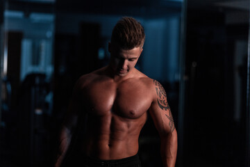 Fototapeta na wymiar Muscular bodybuilder guy standing on gym in the dark