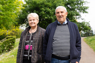 Senior couple walking in the park posing for camera. Elder woman holding husband's arm outdoors. Company, support concepts