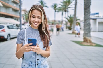Fototapeta premium Young caucasian girl smiling happy using smartphone at the city.