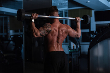 Fototapeta na wymiar Athletic strong bodybuilder man with bare back and muscles doing exercise in the gym at night