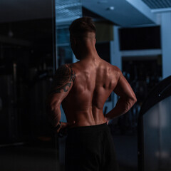 Fototapeta na wymiar young handsome sports guy with a muscular naked torso stands with his back to the camera in the sport gym