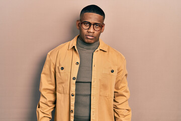 Young black man wearing casual clothes and glasses with serious expression on face. simple and natural looking at the camera.