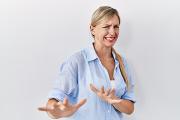 Beautiful blonde woman standing over white background disgusted expression, displeased and fearful...
