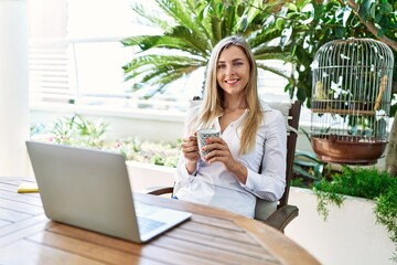 Young blonde woman drinking coffee using laptop working at the terrace.