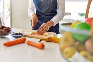 Young blonde woman cutting banana at kitchen