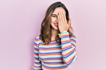 Young hispanic girl wearing casual clothes covering one eye with hand, confident smile on face and surprise emotion.
