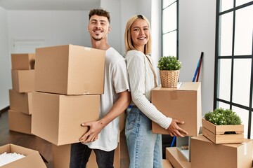 Young caucasian couple smiling happy holding cardboard boxes standing at new home.