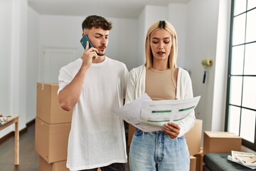 Young caucasian couple reading document and talking on the smartphone at new home.