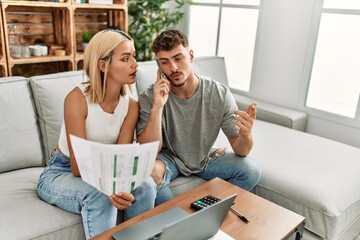 Young caucasian couple with serious expression controlling family economy using laptop and smartphone at home.